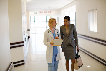 Doctor and businesswoman walking in hospital corridor