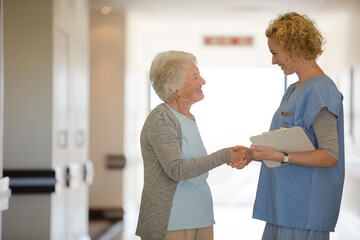 Fototapeta premium Nurse and senior patient shaking hands in hospital corridor