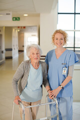 Nurse helping senior patient with walker in hospital corridor