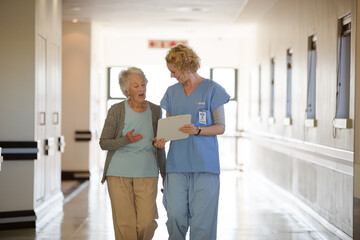 Nurse and aging patient reading chart in hospital corridor