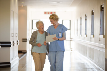 Nurse and aging patient reading chart in hospital corridor