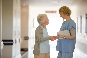 Fototapeta premium Nurse and senior patient shaking hands in hospital corridor