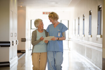 Obraz premium Nurse and aging patient reading chart in hospital corridor