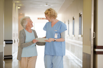 Nurse and aging patient reading chart in hospital corridor
