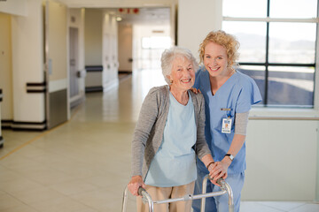 Fototapeta premium Nurse helping senior patient with walker in hospital corridor