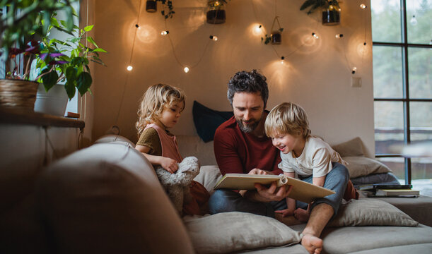 Mature father with two small children resting indoors at home, looking at photo album.