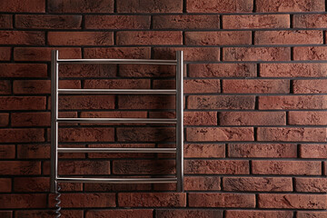 Modern heated towel rail on red brick wall. Space for text