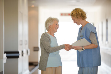Obraz premium Nurse and senior patient shaking hands in hospital corridor