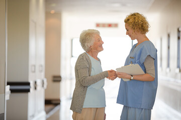 Fototapeta premium Nurse and senior patient shaking hands in hospital corridor