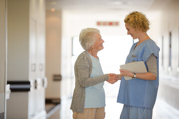 Nurse and senior patient shaking hands in hospital corridor