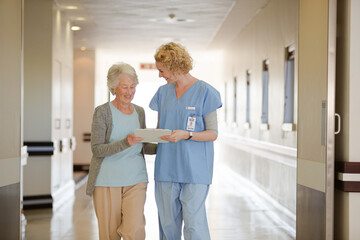 Nurse and aging patient reading chart in hospital corridor