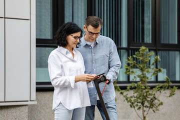 Fototapeta premium Senior couple using electric scooter for transportation in a modern city environment. Healthy senior lifestyle outdoors