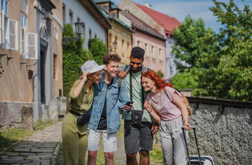 Obraz premium Group of young people outdoors on trip in town, using online map on smartphone.