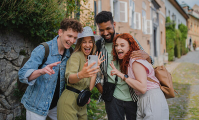 Portrait of group of young people outdoors on trip in town, taking selfie with smartphone.