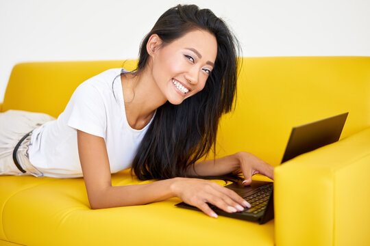 Pretty Smiling Woman Using Laptop Lying At Cozy Yellow Couch On White Background