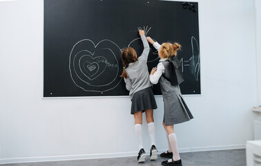 Lively schoolgirls having fun, drawing different shapes on a blackboard.