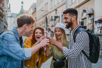 Front view of group of happy young people with drinks outdoors on street on town trip, laughing.