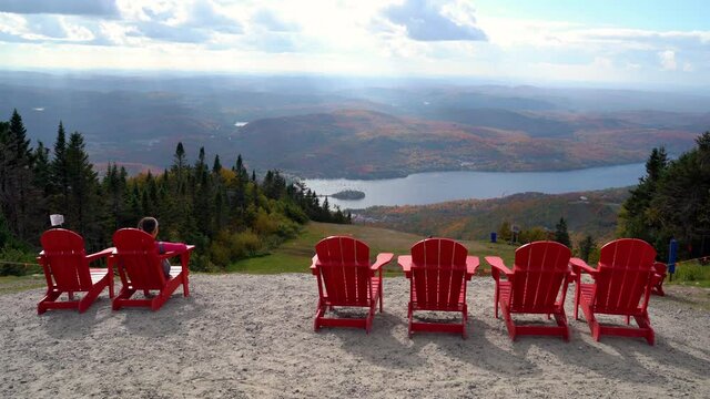 Mont Tremblant, Laurentians, Quebec, Canada. Classic red chairs at Viewpoint with Autumn Fall Foliage Colorful Forest. Hiking Woman Resting on Mountain Summit