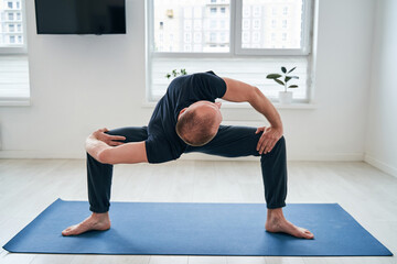 Strong muscular man standing on fitness mat in living room and stretching her body