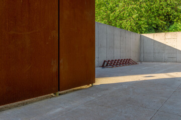 Wall made of architectural concrete and corten sheet surrounded by greenery in the park, a bicycle rack standing on a concrete floor
