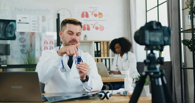 Telemedicine concept where good-looking confident smart experienced bearded doctor explaining for online audience through camera how to use pulse oximeter