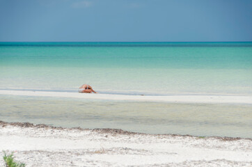 A young woman on the tropical beach in a yoga pose, in the background the Caribbean Sea of Holbox Island in Mexico