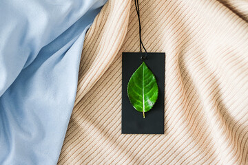 Green leaf on clothing tag and organic fabric background, sustainable fashion and brand label...