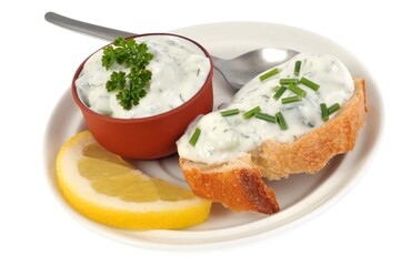 Tartine de tzatziki avec de la ciboulette dans une assiette avec une rondelle de citron en gros plan sur fond blanc