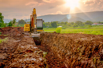 Backhoe or excavator working on land of countryside, excavator dig soil in rice field site industry, blue sky and green field agriculture background