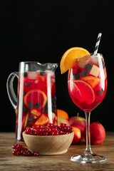 Glass and jug of Red Sangria with fruits on wooden table against black background