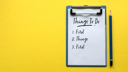 Top view of a pencil and a clipboard with paper written with Things To Do and a number with sentence First Things First on a yellow background with copy space.
