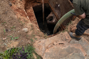 Man pumping sludge from a newly opened septic tank, horizontal aspect