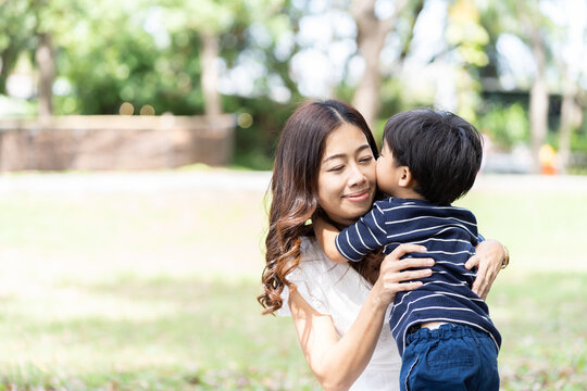 Asian little boy playing and kissing his mother outdoor in the park. Happy mother having fun with her little son outdoor. Young mom spending time with her son on holiday in the garden. people, family