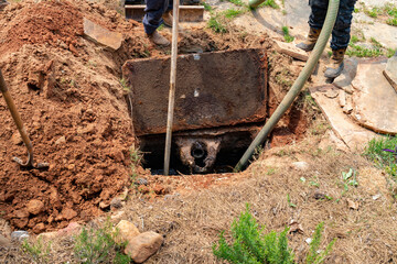 Septic tank being pumped of sludge, lid pulled back to provide access, horizontal aspect