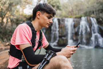 Traveling man drinking from hydration pack near waterfall in woods