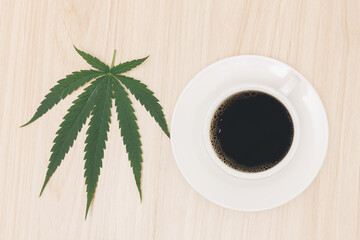 Hot black coffee in a cup with a white saucer on a wooden table and decorated with hemp leaves, cannabis coffee relaxing drink concept.flat lay,top-down,top view.