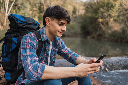 Smiling traveling man using smartphone during hike