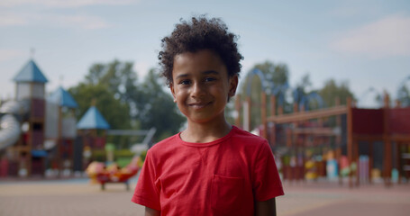 Medium shot of african active little boy on playground looking at camera