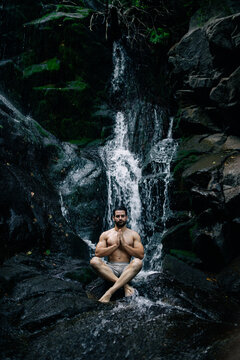 Relaxed man meditating near waterfall