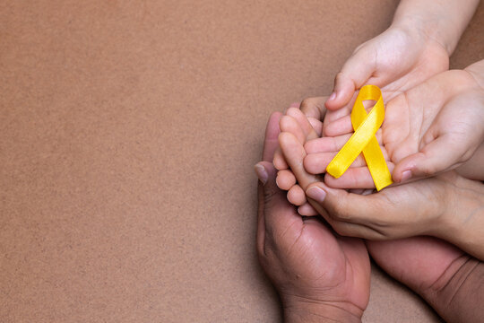 hands holding yellow ribbon, childhood cancer, chocolate background