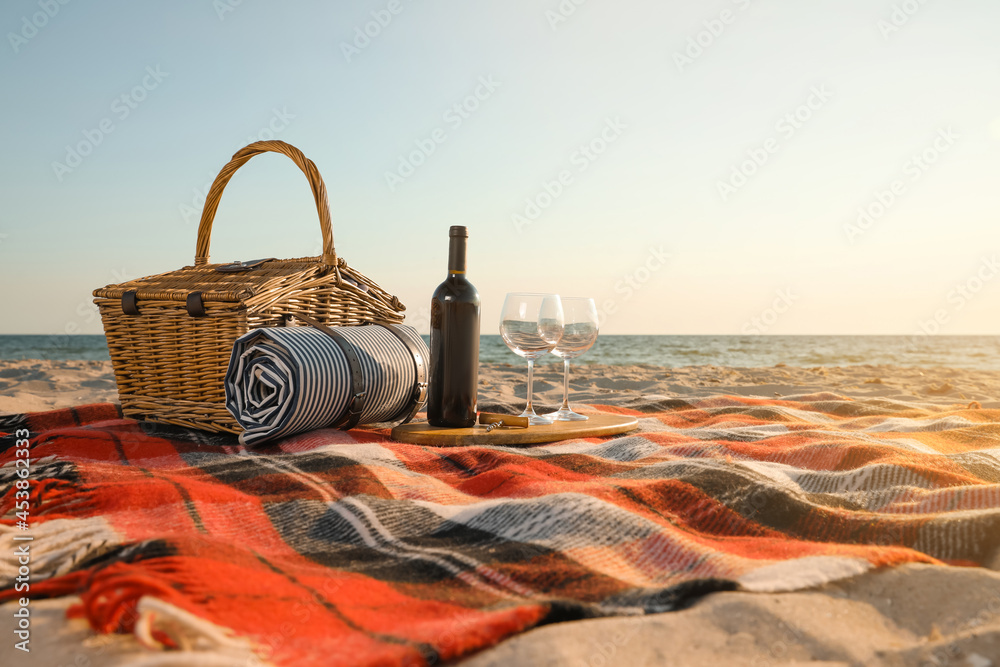 Canvas Prints Blanket with picnic basket, bottle of wine and glasses on sandy beach near sea, space for text