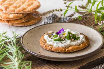 Round crispbread with herbal cream cheese and fresh herbs on a wooden board