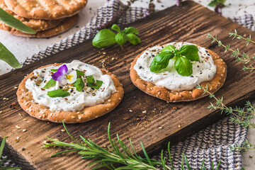 Round crispbread with herbal cream cheese and fresh herbs on a wooden board
