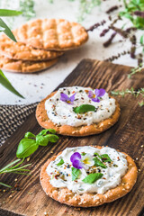 Round crispbread with herbal cream cheese and fresh herbs on a wooden board, vertical