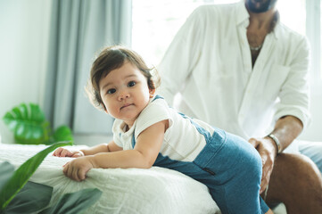 Fototapeta premium Cute little playful girl child learning to walk and stand by taking support of couch at home while looking away mischievously