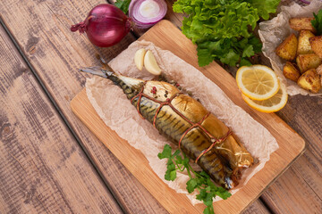 Composition smoked mackerel fish with garnish potatoes lemon greens onions served on wooden board plate top view