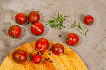 Fresh organic ripe red cherry tomatoes on the kitchen counter and bamboo board. Top view. Branches of rosemary and pepper as a decoration. 