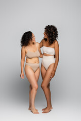 Smiling african american women in lingerie hugging on grey background, body positive concept