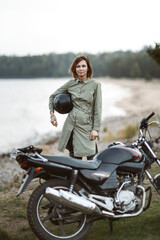 Fototapeta na wymiar Portrait of a female biker standing outdoors. A woman holds a helmet in her hands on the background of a motorcycle.
