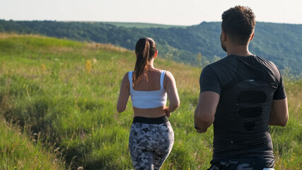 The man and woman jogging along the green hill